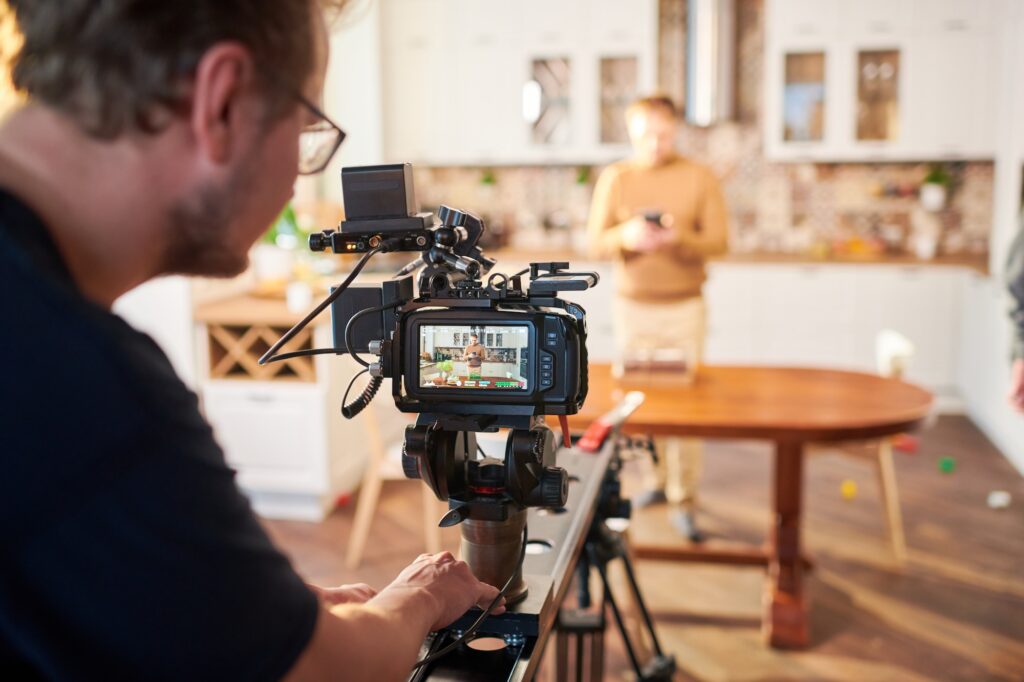 Young male videographer standing by video camera while shooting advertisement